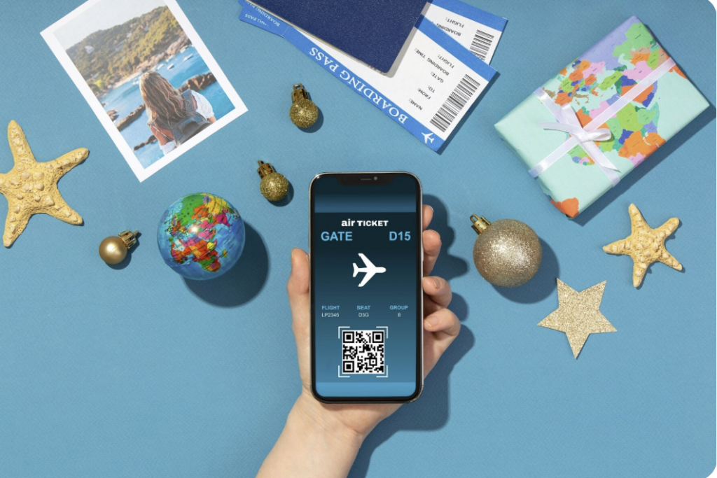 Main tenant un smartphone affichant une carte d’embarquement numérique, entourée d’éléments de voyage : photo de vacances, globe terrestre, passeport, billets d’avion, décorations dorées et paquet cadeau sur fond bleu.