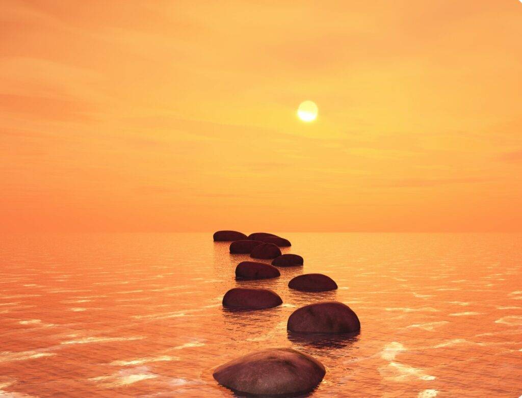 Alignement de pierres sur une mer calme sous un ciel orange au coucher du soleil