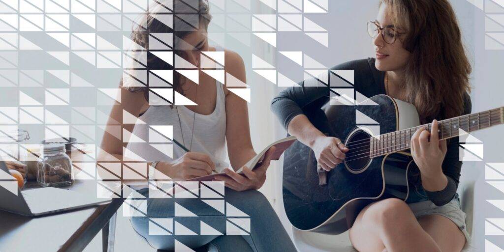 Femme jouant de la guitare pendant qu’une autre écrit dans un carnet, collaboration musicale dans un cadre décontracté