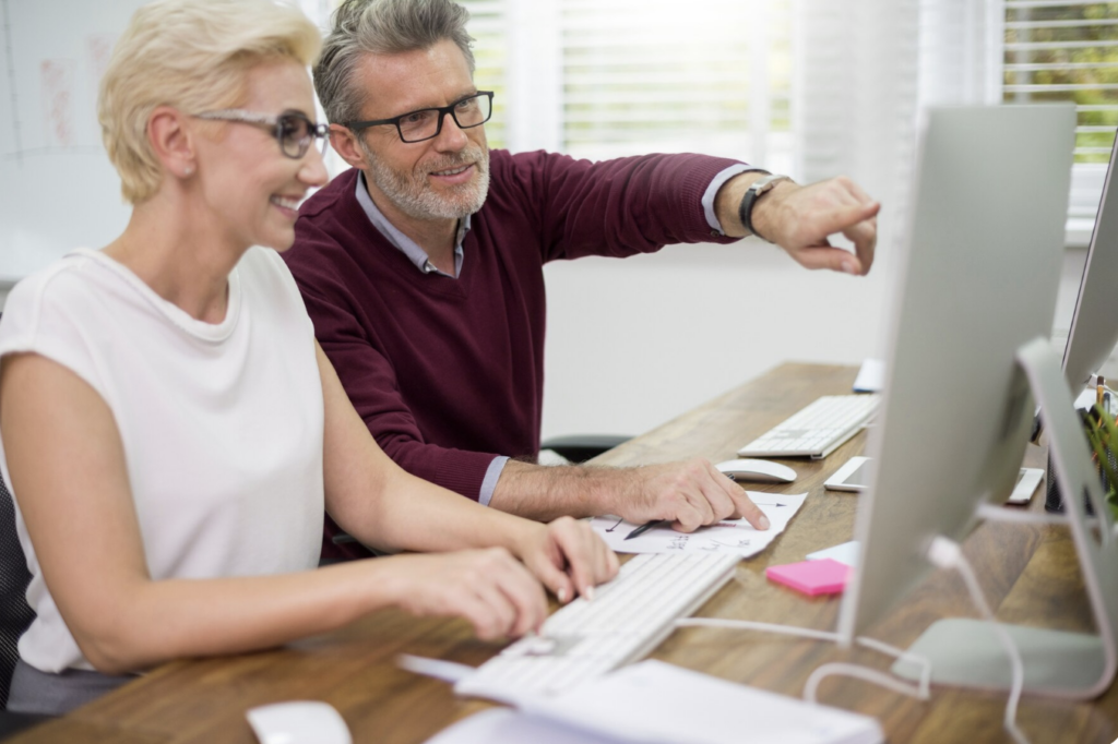Deux personnes de 50 ans collaborant sur un projet numérique, valorisation de compétences devant un ordinateur dans un cadre professionnel.