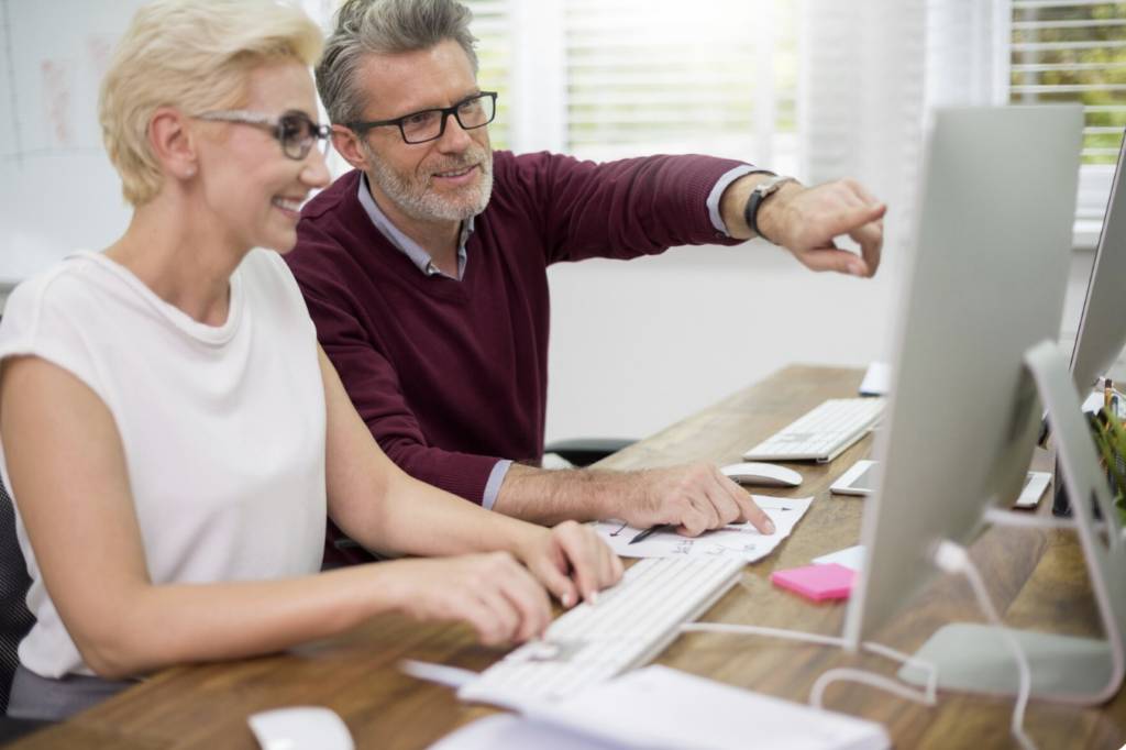 Deux personnes de 50 ans collaborant sur un projet numérique, valorisation de compétences devant un ordinateur dans un cadre professionnel.